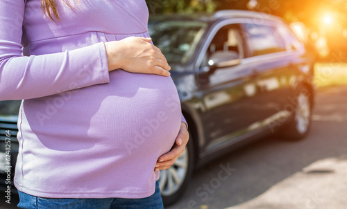 A pregnant girl with a big belly in a purple sweater on the background of a car. The concept of travel and a long trip in a car during pregnancy. Copy space for text © HENADZY