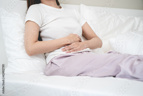 Close-up woman feeling stomach pain from cycle period on the bed at home.