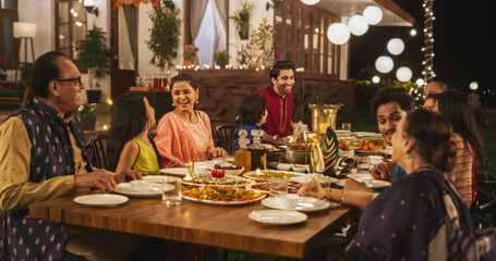 Happy Extended Indian Family Dining Together Outdoors in Fancy House Garden at Night. Family Members Laughing and Sharing Funny Stories and Memories While Eating Delicious Food