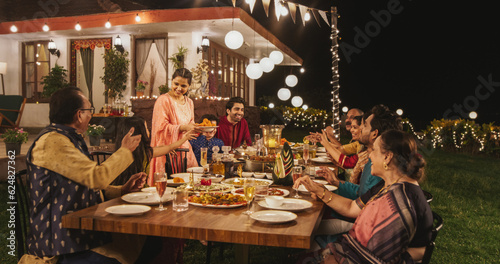 Photo Big Family Celebrating Diwali: Indian Family in Traditional Clothes Gathered Together on a Dinner Table in a Backyard Garden Full of Lights