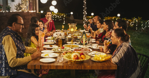 Family Time and Good Happy Memories: Indian Relatives of All Ages Gathered Together Around Dinner Table on a Backyard Garden Party to Eat Traditional Food. Moment of Pure Love and Sharing