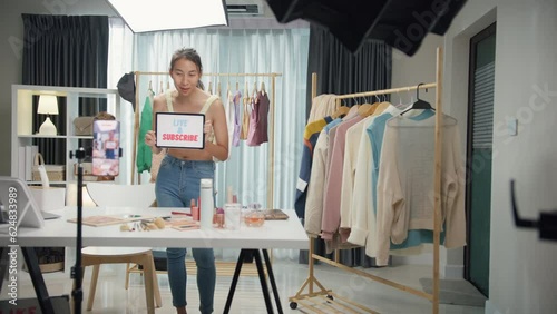 Young Asia lady beauty blogger wear crop top looking at phone camera live stream use digital tablet talk follower introduce her chanel ask audience like subscribe share her chanel at house studio.