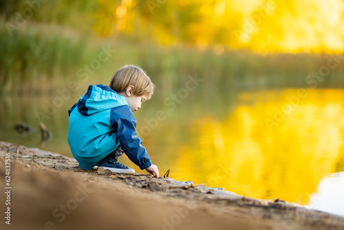 Adorable toddler boy having fun by the Gela lake on sunny fall day. Child exploring nature on autumn day in Vilnius, Lithuania.