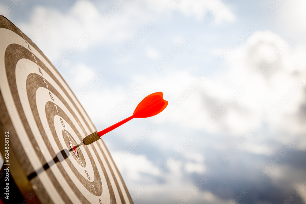 Close up shot red darts arrows in the target of dartboard center on dark blue sky background. Business target or goal success and winner concept. Close up shot red darts arrows in the target of dartboard center on dark blue sky background. Business target or goal success and winner concept.