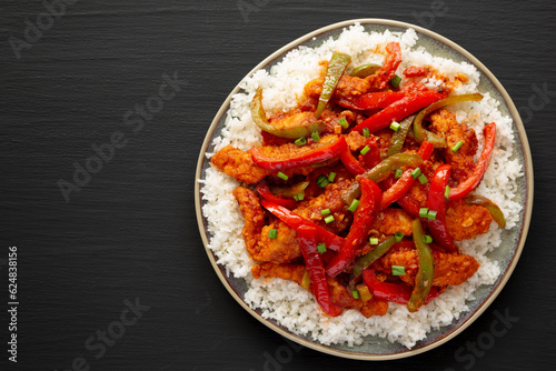 Homemade Simple Chili Chicken with White Rice on a Plate on a black background, top view. Flat lay, overhead, from above.