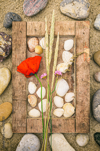 Bilderrahmen aus Treibgut im Sand mit Muscheln, Steinen und Blumen dekoriert liegt am Strand im Urlaub photo