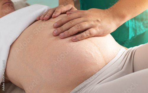 A chiropractor makes a massage to a pregnant girl for an easy delivery, close-up. © HENADZY