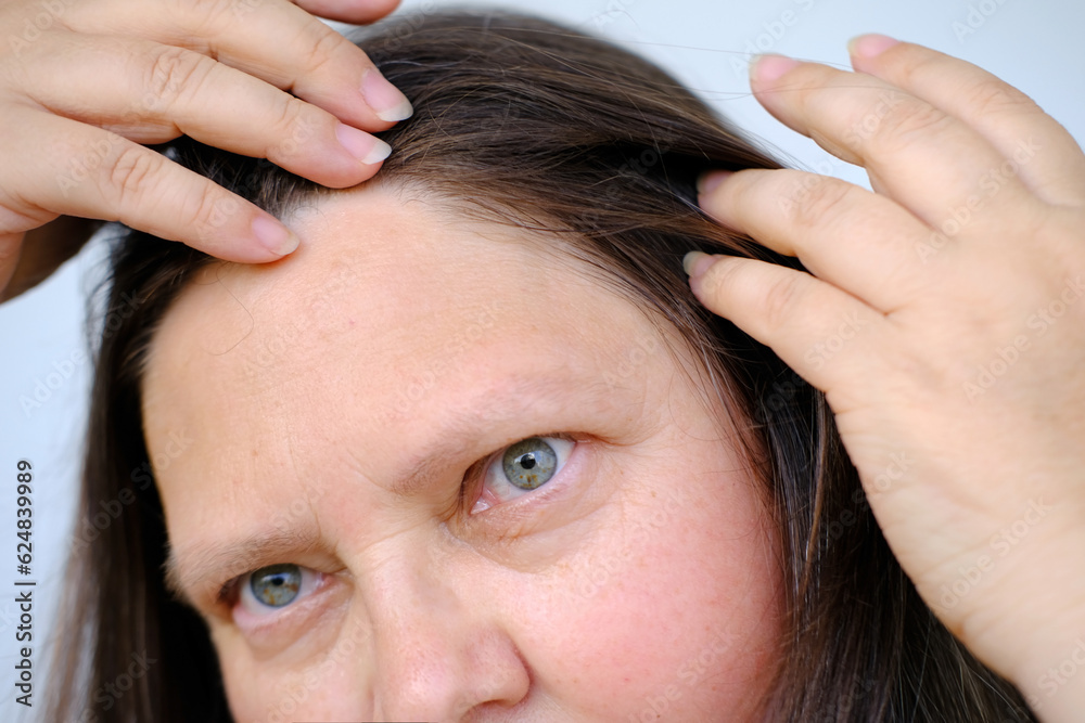 close up middle-aged female face, woman 45-50 years old looks gray hair, carefully examines hair, Aging with grace, age-related changes, Self-esteem and self-image at any age, Hair grooming close up middle-aged female face, woman 45-50 years old looks gray hair, carefully examines hair, Aging with grace, age-related changes, Self-esteem and self-image at any age, Hair grooming