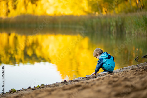 Adorable toddler boy having fun by the Gela lake on sunny fall day. Child exploring nature on autumn day in Vilnius, Lithuania. photo