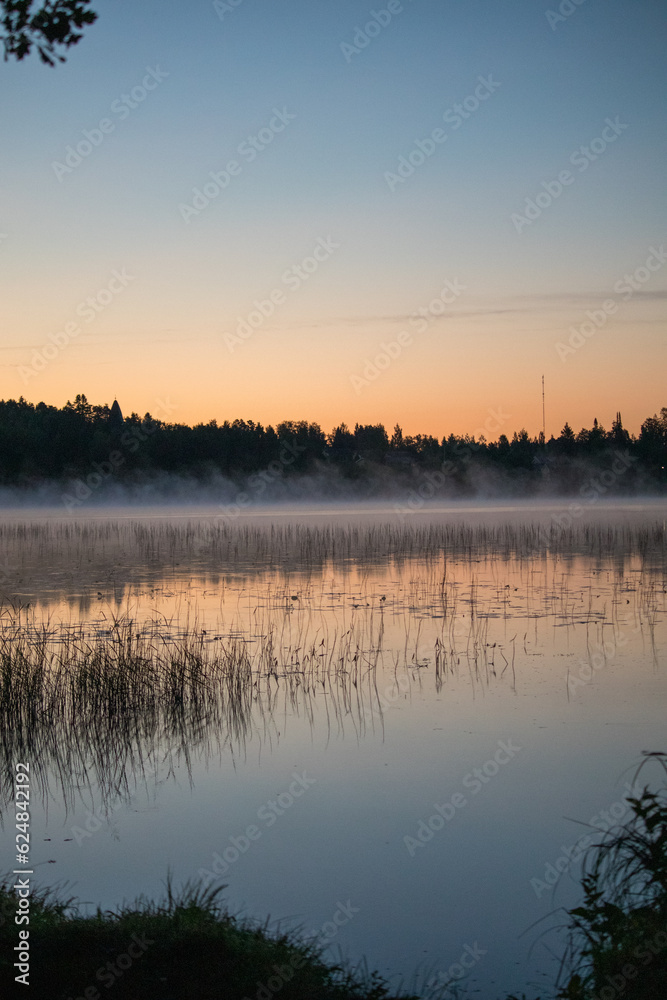 Sunrise on a misty still lake in summer countryside.