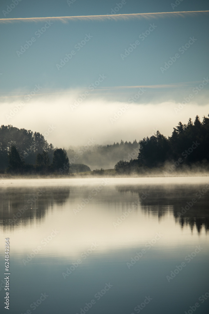 Lake scenery with a misty clouds reflecting over a forest horizon.