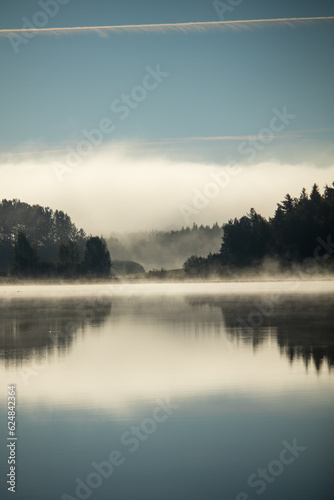 Lake scenery with a misty clouds reflecting over a forest horizon.