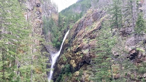 View from the roadside and metal bridge panning to Gorge Creek Falls cascading from high up the mountain - North Cascades National Park, Washington, USA photo