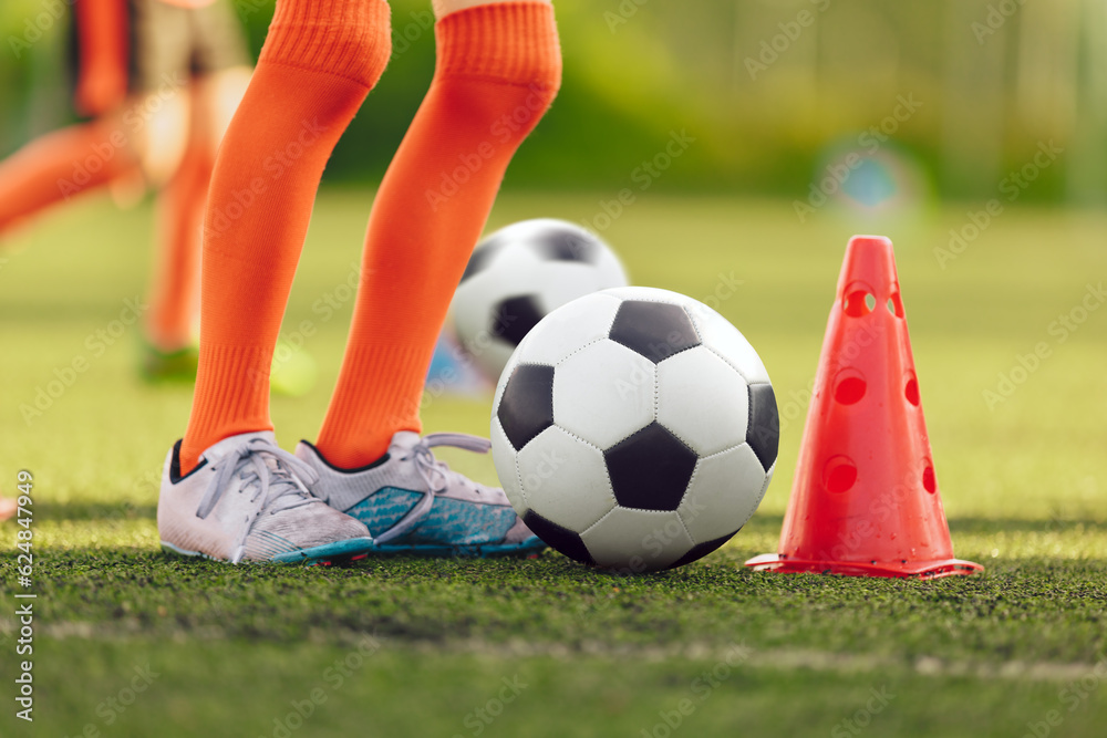 Fototapeta premium Legs of youth soccer player on training drill. Football summer training camp for children. Kids play football during training session on grass pitch