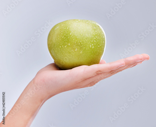 Vegan, hand and apple with water drops, nutrition and clean against a grey studio background. Zoom, fingers and person with a fruit in a palm, detox and snack for diet with self care and wellness