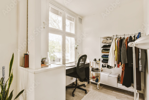a room with a desk, chair and clothes hanging on the wall behind it is a large window that looks out onto the street © Casa imágenes