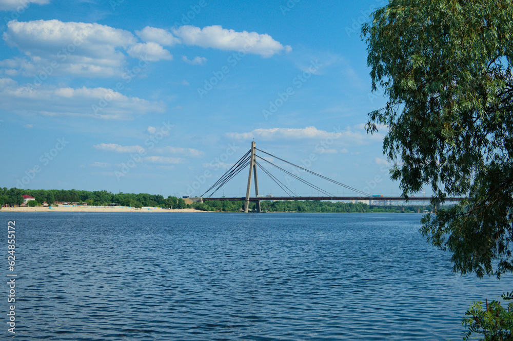 Obraz premium Panoramic landscape view bridge across Dnipro River in Kyiv, Ukraine. Pivnichnyi (Northern) bridge, cable-stayed bridge across the Dnipro. Infrastructure of a big city concept. Sunny summer day