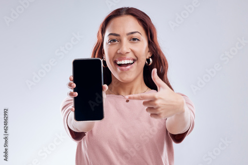 Happy woman is pointing at phone screen, mockup and marketing, mobile app ads on white background. Website promo, advertising and female ambassador in portrait with social media branding in studio photo