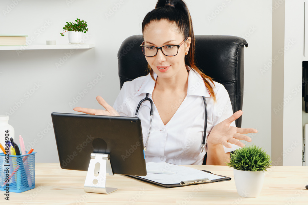 A girl doctor conducts a consultation from her office via video link using a tablet. A girl doctor conducts a consultation from her office via video link using a tablet.