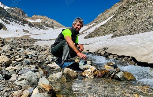 Hiker fills his water bottle from a high mountain stream.