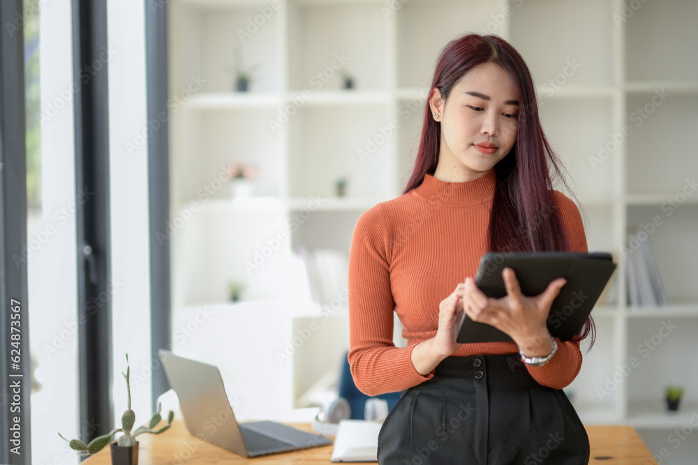 Asian Female using digital tablet and standing in the workplace Asian Female using digital tablet and standing in the workplace