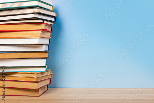 Stack of books in the colored cover lay on the wooden  table and blue backround. Education learning concept