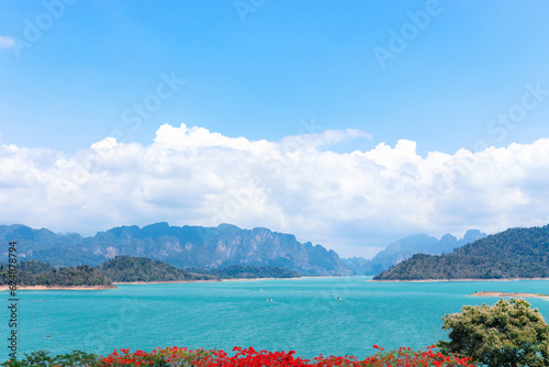 Beautiful point view of Ratchaprapa Dam or Cheow Lan Dam, crystal clear blue freshwater lake with mountains and cloudy sky as background, popular tourist attractions in Surat Thani province, Thailand.