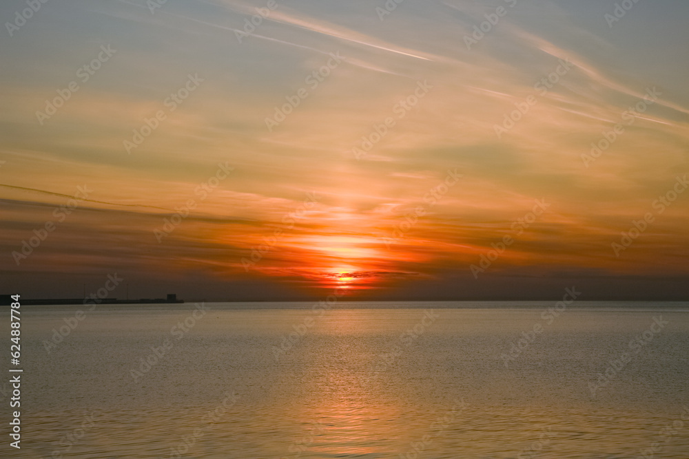 the sun setting in the clouds, reflected in the surface of the water surface of the sea