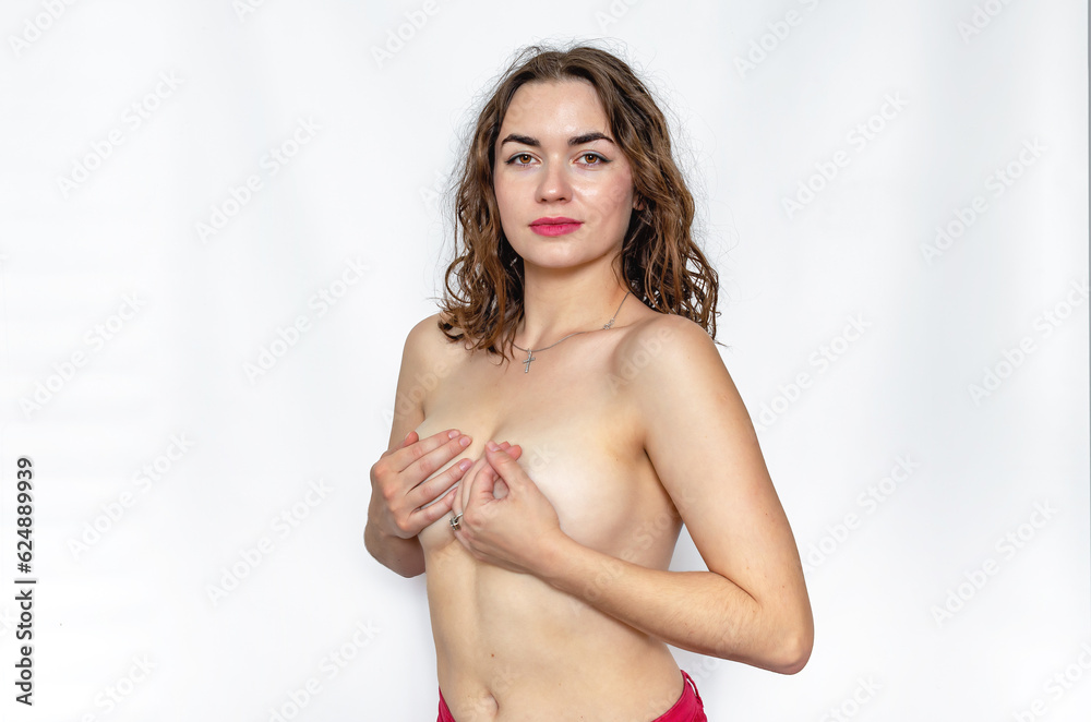Large bare female breasts, which the woman covers with her hands. Sensual lips, wavy hair.