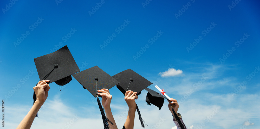 Fototapeta premium Many hands holding graduation hats against blue sky