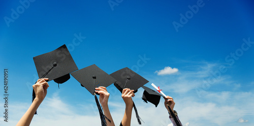 Obraz na plátně Many hands holding graduation hats against blue sky