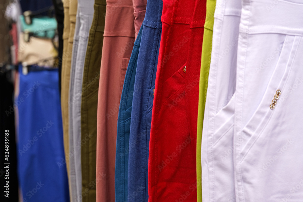 Multi-colored trousers hang on hangers in a women's clothing store.