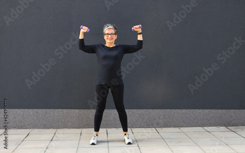 Morning exercises of a sporty mature woman with dumbbells in her hands. © Andrii Zastrozhnov