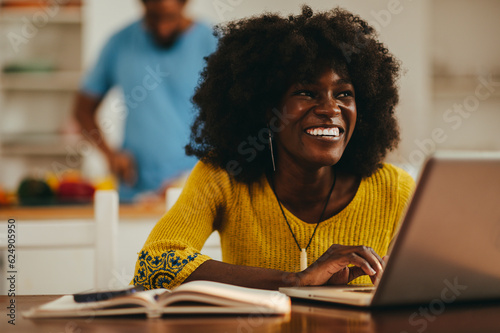A happy interracial woman is using a laptop for remote work from home.