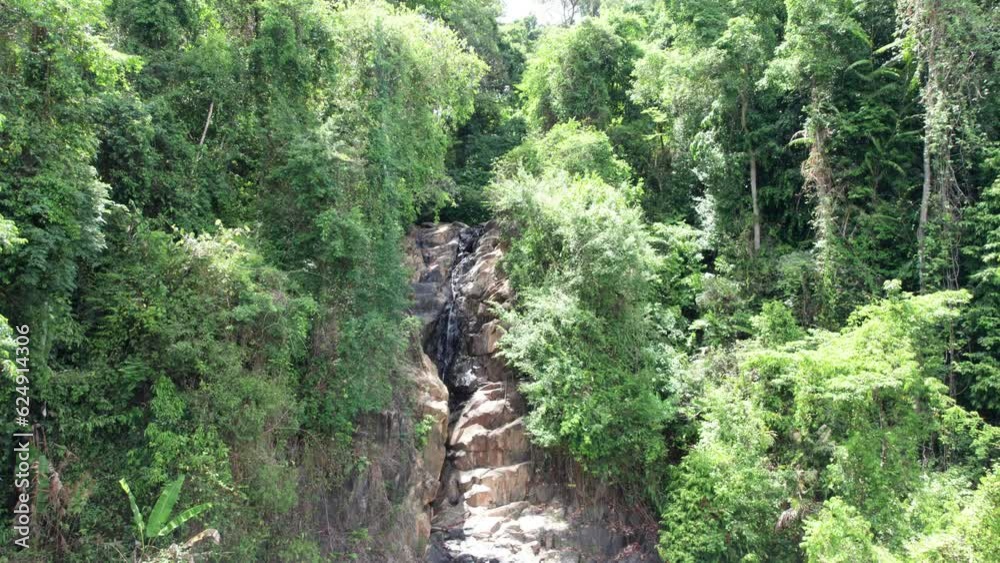 A small waterfall among rocks and green jungle. A small lake with a reflection of clouds in the sky. Lots of trees. High cliffs and big rocks. Shadows from trees. Top view from drone. Thailand, Phuket A small waterfall among rocks and green jungle. A small lake with a reflection of clouds in the sky. Lots of trees. High cliffs and big rocks. Shadows from trees. Top view from drone. Thailand, Phuket