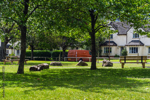 Idyllic English country house, lush green lawn, dappled sunlight through trees, wooden bench, vintage red car, old house walls in the background.