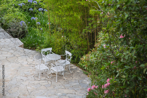Mediterranean garden design and landscaping, Provence,France:Beautiful resting place on a virgin stone-flagged terrace, table and four chairs, lush green plants, bamboo, oleander and agapanthus lilies
