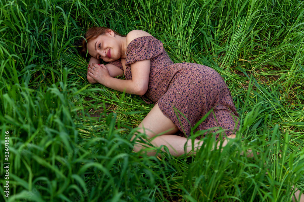 A young girl in a beautiful dress lies in the green grass A young girl in a beautiful dress lies in the green grass