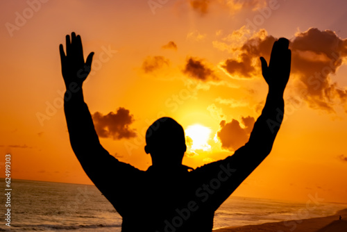 An evocative depiction of a Christian worshipper, his silhouette illuminated by the breathtaking sunset of the solstice, as he surrenders to Jesus in heartfelt prayer.