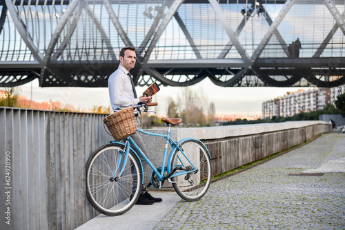 Business man with vintage bicycle by the river reading a book