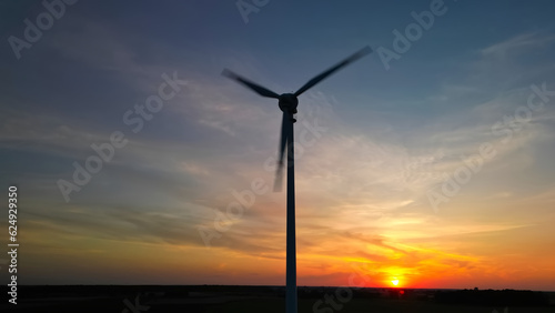 Aerial, low angle view of the silhouette of a wind turbine with blurred wings on sunset. Production of clean ecological green electricity by windmills. 