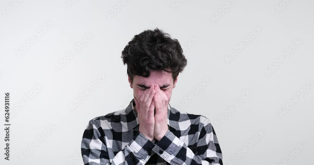 Caucasian man stands against a pure white background, his emotions laid bare. He finds solace in vulnerability, as tears stream down his face and he delicately shields his visage with trembling hands. Caucasian man stands against a pure white background, his emotions laid bare. He finds solace in vulnerability, as tears stream down his face and he delicately shields his visage with trembling hands.