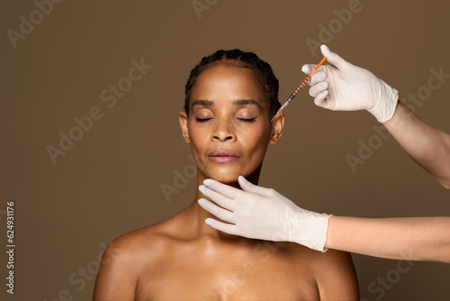 Cosmetic beauty injections concept. Attractive black middle aged woman getting facial injection in cheekbones zone photo