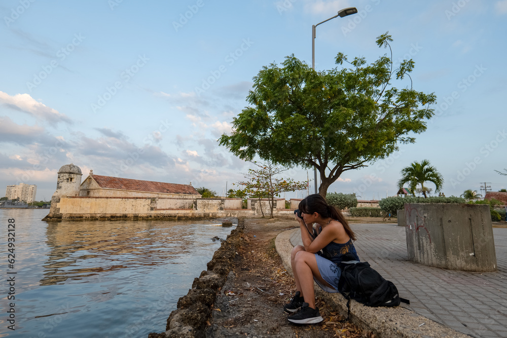 Peruvian Woman Sits on the Sidewalk and Takes a Picture of Cartagena Landscape