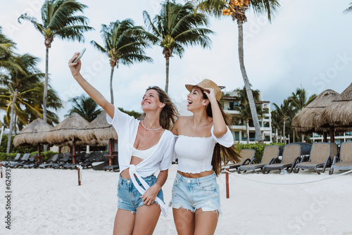 latin woman taking photo selfie with mobile phone to female friend at caribbean beach in Mexico Latin America, hispanic young female