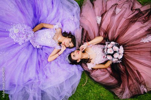 Portrait of Mexican quinceanera teenagers lying on the grass looking into each other's eyes photo