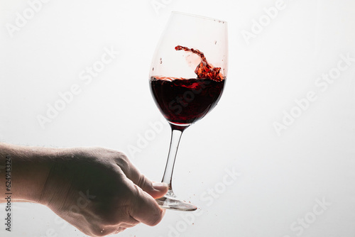 glass of red wine in motion with the glass held at the base by a man's hand