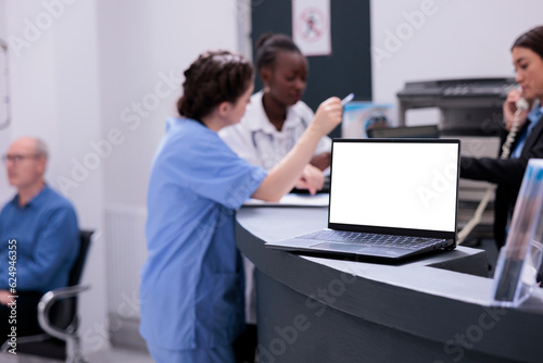 Medical staff working at patient treatment discussing disease symptoms during checkup visit consultation in hospital waiting area. Laptop computer with white screen standing on counter desk