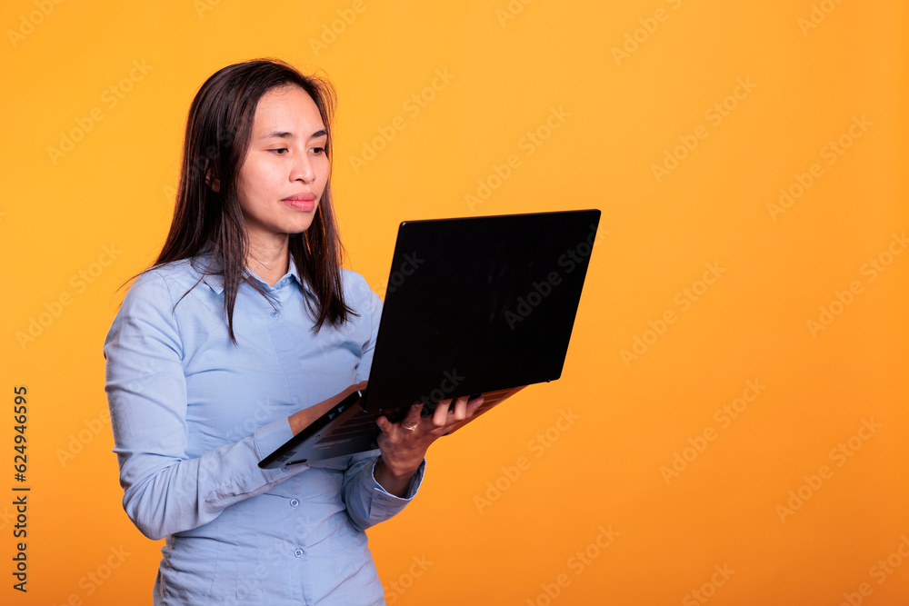 Fototapeta premium Asian woman using digital device browsing webpages on internet, searching information for research project. Young adult using laptop computer to navigate on social media. Remote work concept