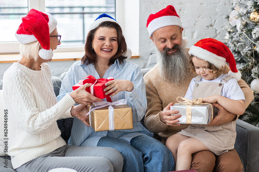 Fototapeta premium Happy smiling family near beautiful Christmas new year tree exchanging gifts in the morning. Grandmother, grandfather, daughter and granddaughter celebrating holidays at home together